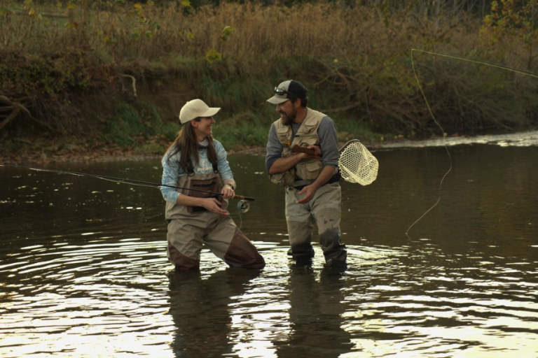 Male Shenandoah National Park fishing guide holding a net standing in the water with female angler smiling as they celebrate a great catching while near Charlottesville, VA fishing.